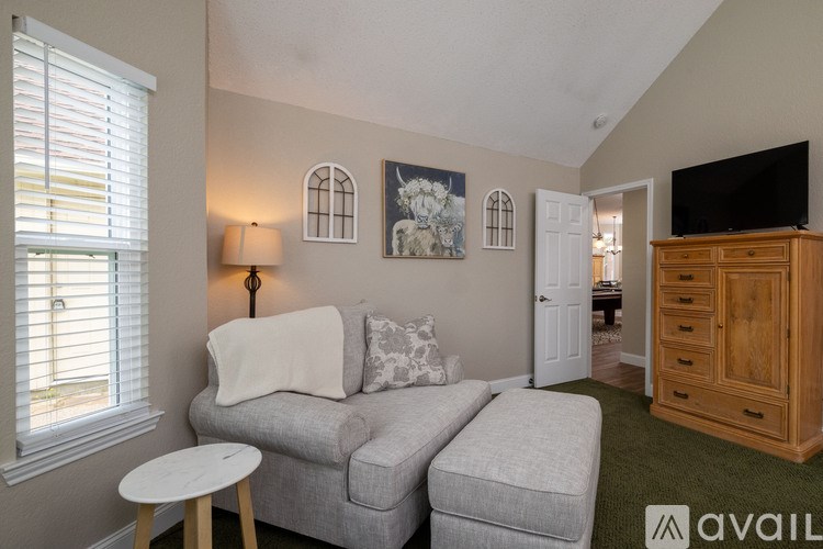 A living room with a grey couch, a white ottoman, a wooden cabinet, and a television.