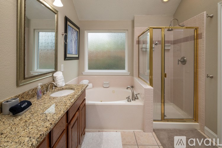 A bathroom with a pink tub and gold fixtures.