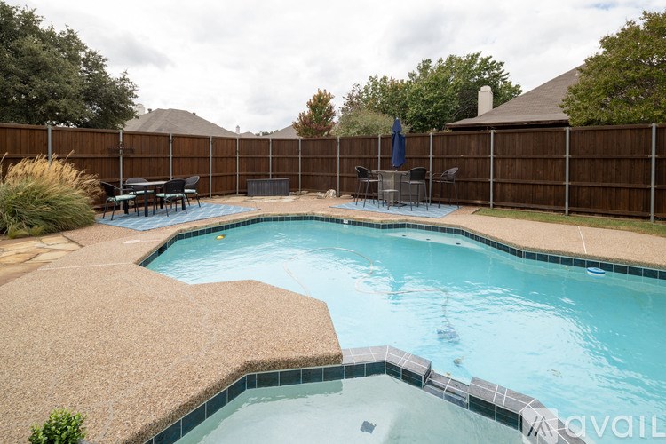 A swimming pool surrounded by a brown fence and a patio area with a table and chairs.