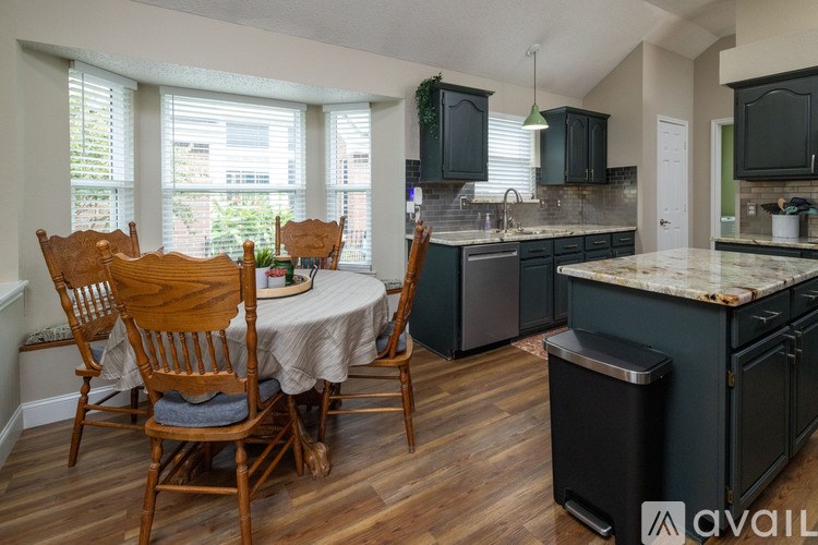 A kitchen with a table and chairs in the foreground and a countertop with a trash can.