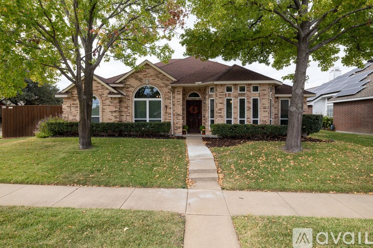 A house with a brown roof and a stone wall is surrounded by a lawn and trees.