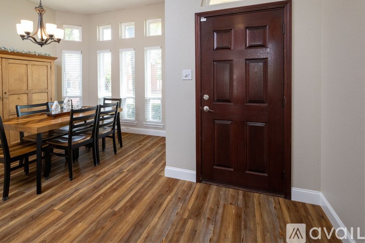 A brown door is in a room with a wooden floor and a table with chairs.
