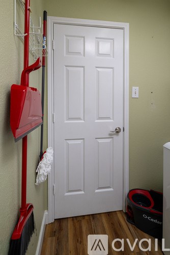 A white door is in a room with a broom and dustpan hanging on the wall.
