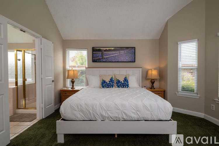 A bedroom with a large bed, two lamps, and a painting on the wall.