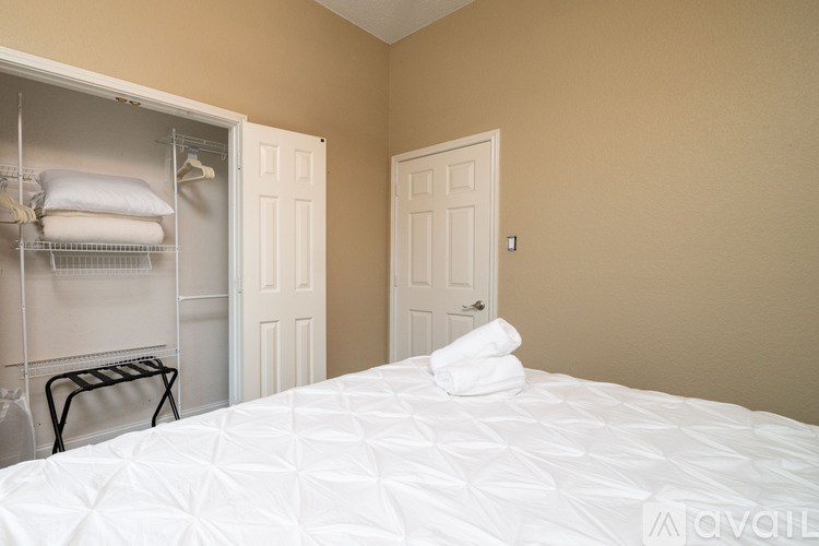 A bedroom with a white bed and a white closet with clothes.