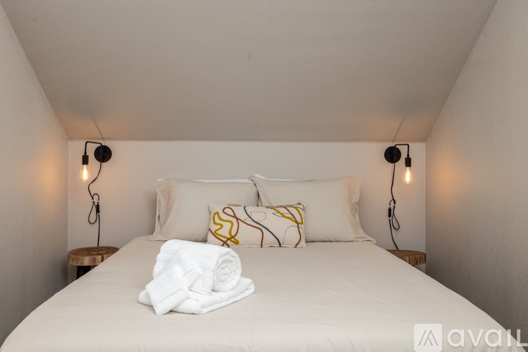 A bed with white bedding and pillows, a white towel, and two lampshades on the bedside tables.