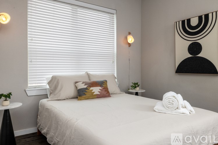 A bedroom with a white bed and a small table with a plant on it.