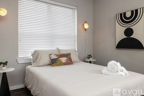 A bedroom with a white bed and a small table with a plant on it.