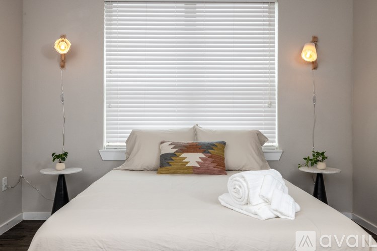A bedroom with a white bed, two lampshades, and a window with blinds.