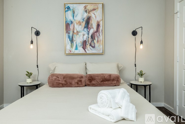 A bedroom with a large bed, two lamps, and a painting on the wall.