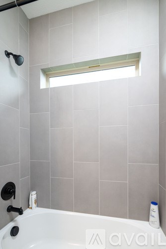 A bathroom with a white tub and grey tiles.