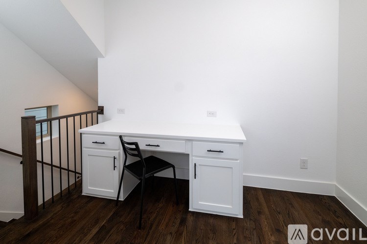 A white desk with a black chair is in a room with wooden floors and white walls.