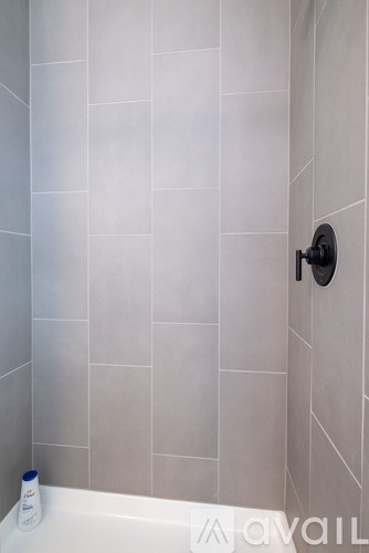 A white tiled shower with a black faucet.