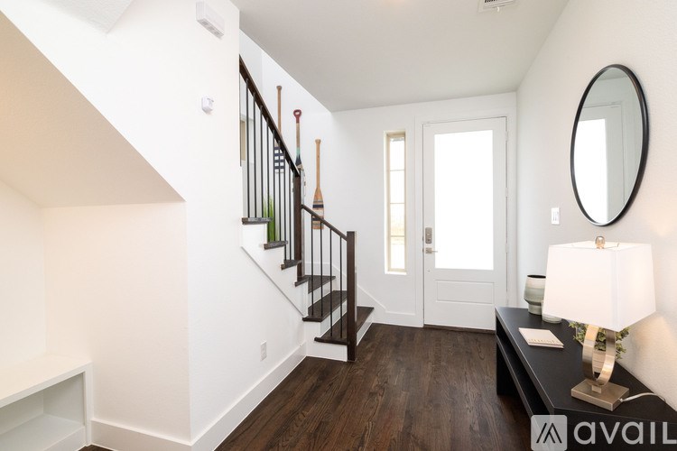 A well-lit hallway with a wooden staircase and a black console table with a lamp on it.