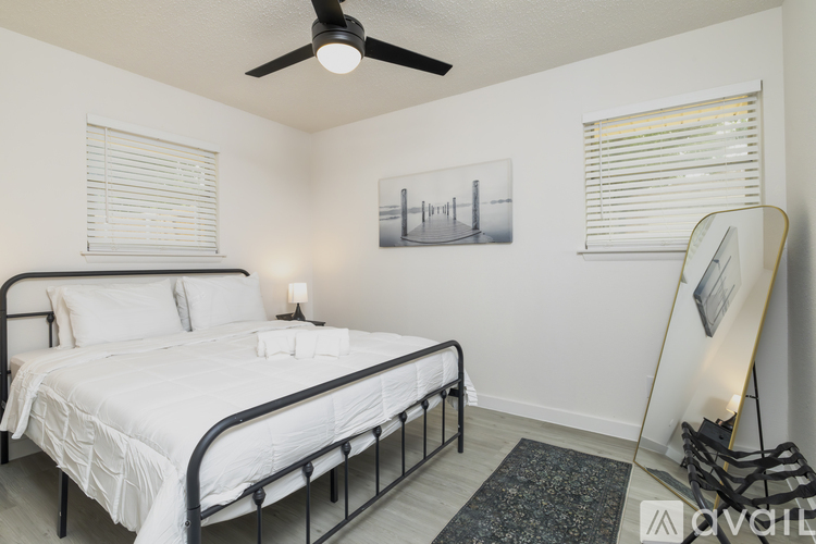 A bedroom with a bed, a ceiling fan, and a painting on the wall.