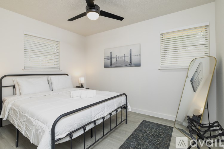 A bedroom with a bed, a ceiling fan, and a painting on the wall.