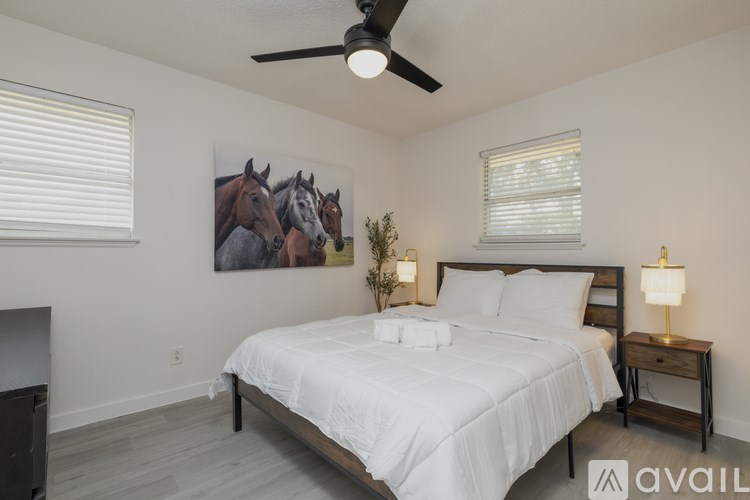 A bedroom with a bed, a ceiling fan, and a painting of horses on the wall.