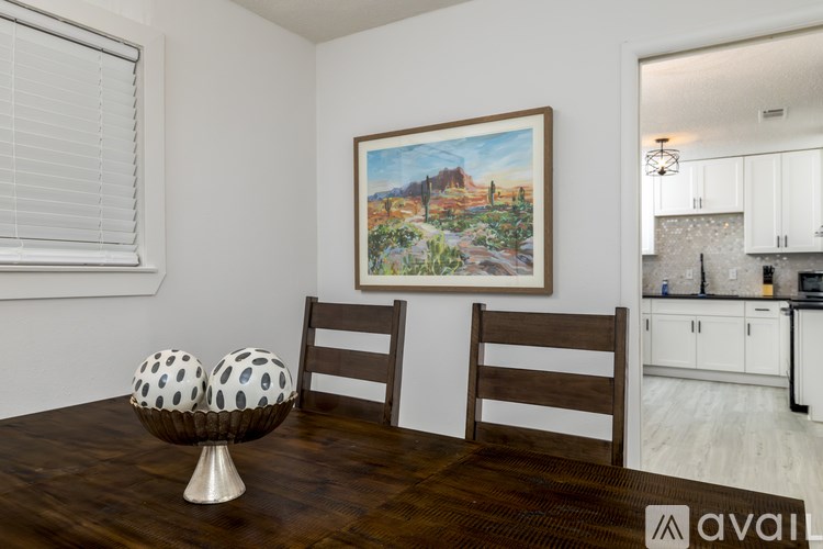 A room with a painting of a desert scene on the wall and a wooden dining table with a bowl and two chairs.