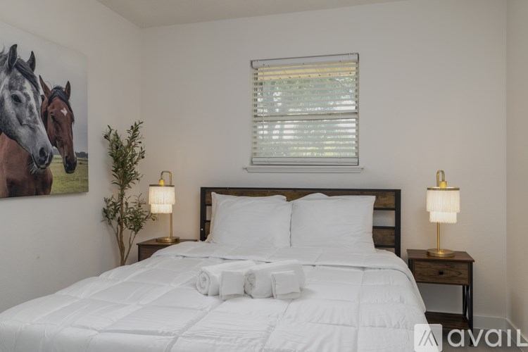 A bedroom with a large bed, two lamps, and a painting of two horses on the wall.