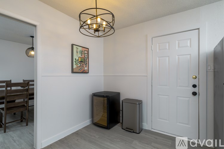 A room with a white door, a grey trash can, and a framed picture on the wall.
