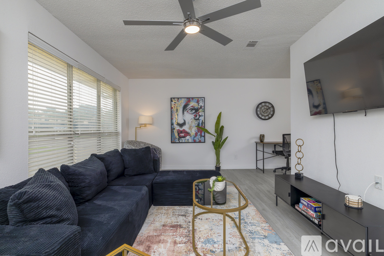 A living room with a grey sofa, a fan, a painting, a plant, and a rug.