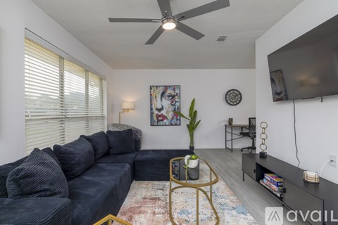 A living room with a grey sofa, a fan, a painting, a plant, and a rug.