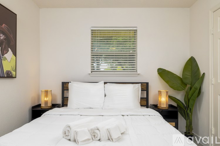 A bedroom with a large bed, two lamps, and a plant.