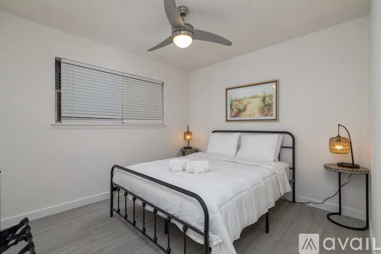 A bedroom with a bed, a ceiling fan, and a painting on the wall.