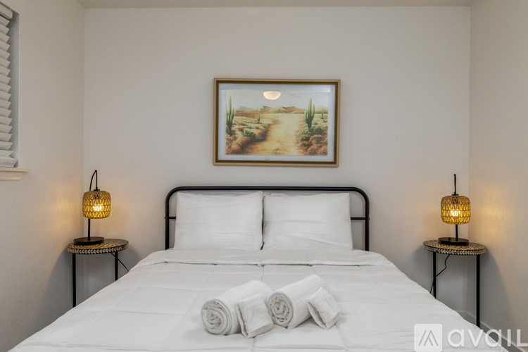 A bedroom with a bed, two lamps, and a painting on the wall.