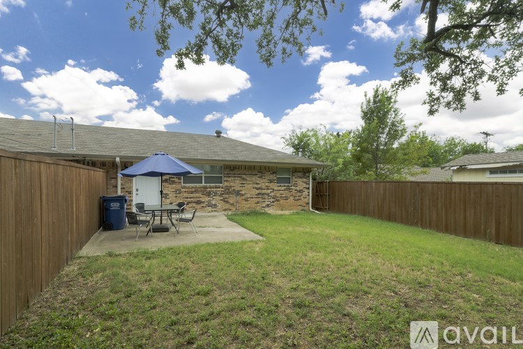 A backyard with a patio and a blue umbrella.