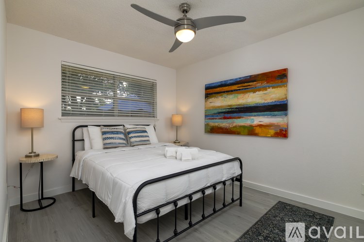 A bedroom with a bed, two lamps, and a painting on the wall.