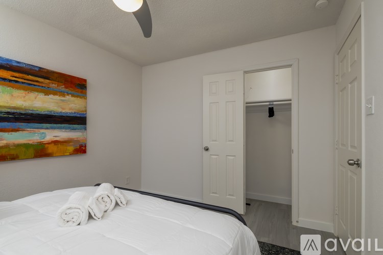 A bedroom with a bed, a ceiling fan, and a painting on the wall.