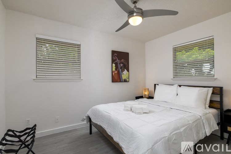 A bedroom with a large bed, a ceiling fan, and a painting on the wall.