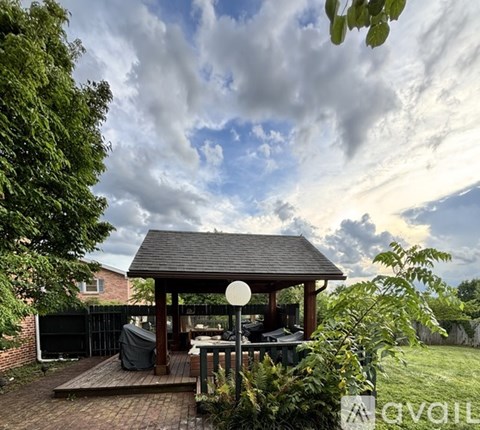 A gazebo is surrounded by a wooden deck and a lush green garden.