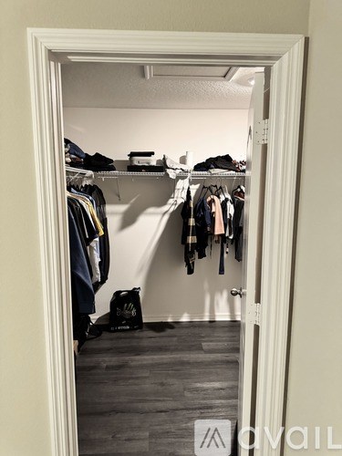 A white door opens to a room with clothes hanging on a rack and a black bag on the floor.