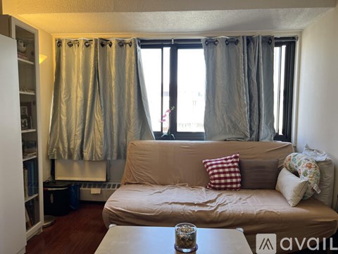A living room with a brown couch and a window with grey curtains.