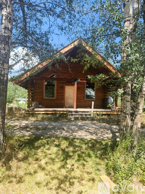 A small wooden cabin sits in a grassy area with trees around it.