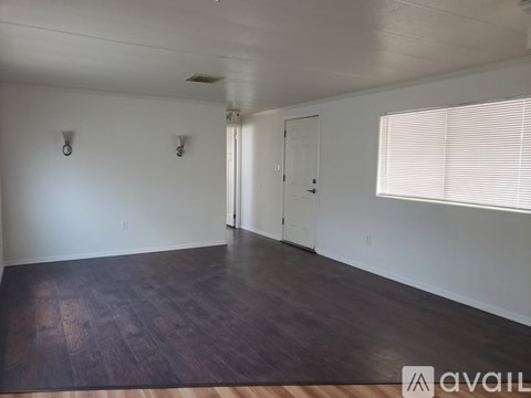 A room with wooden floors and white walls, with a door and a window with blinds.