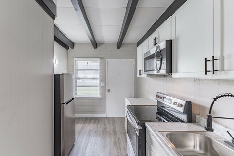 A kitchen with a refrigerator, microwave, oven, and sink.