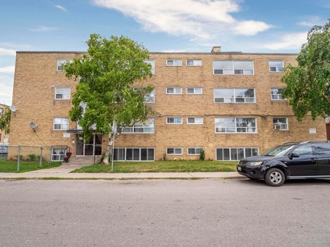 A black car is parked in front of a brick apartment building.