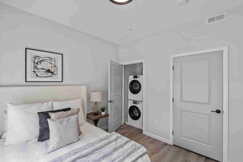 A bedroom with a bed, pillows, a nightstand with a lamp, and a framed picture on the wall.