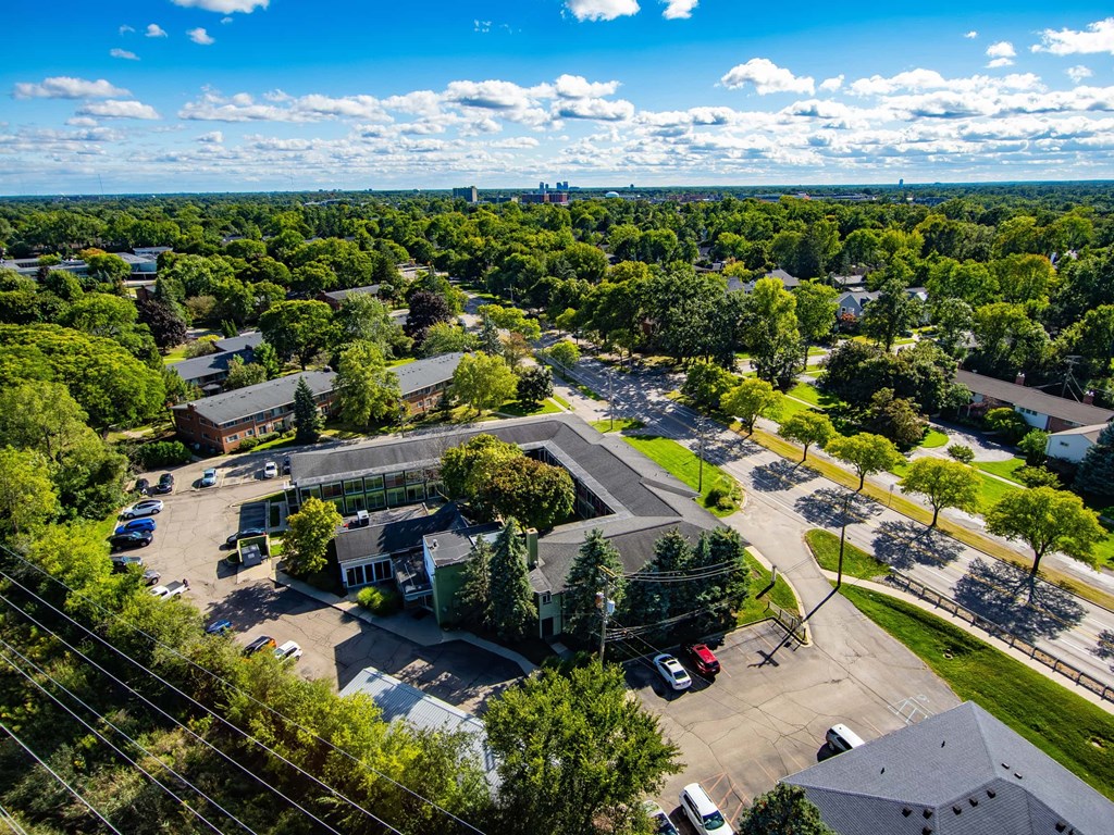 A bird's eye view of a residential area with houses, trees, and a parking lot.