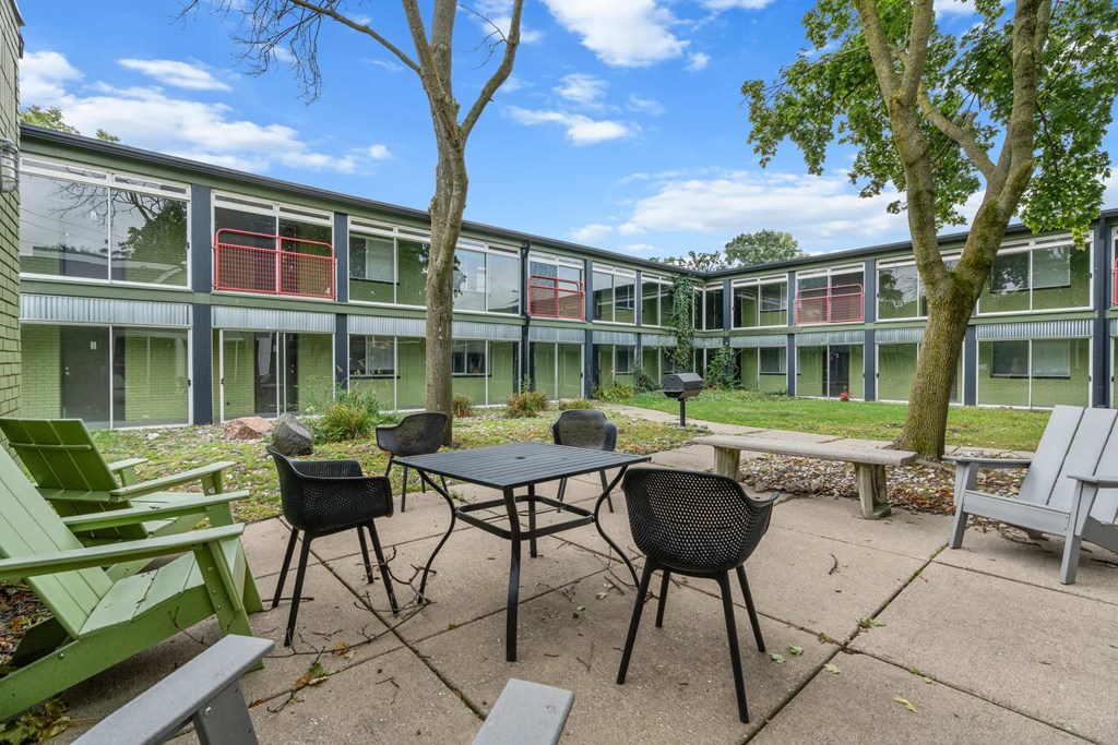 A patio with a table and chairs is surrounded by trees and a building.