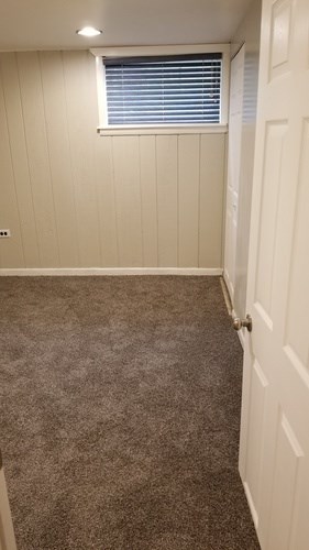 A carpeted hallway with a white door and a window with blinds.