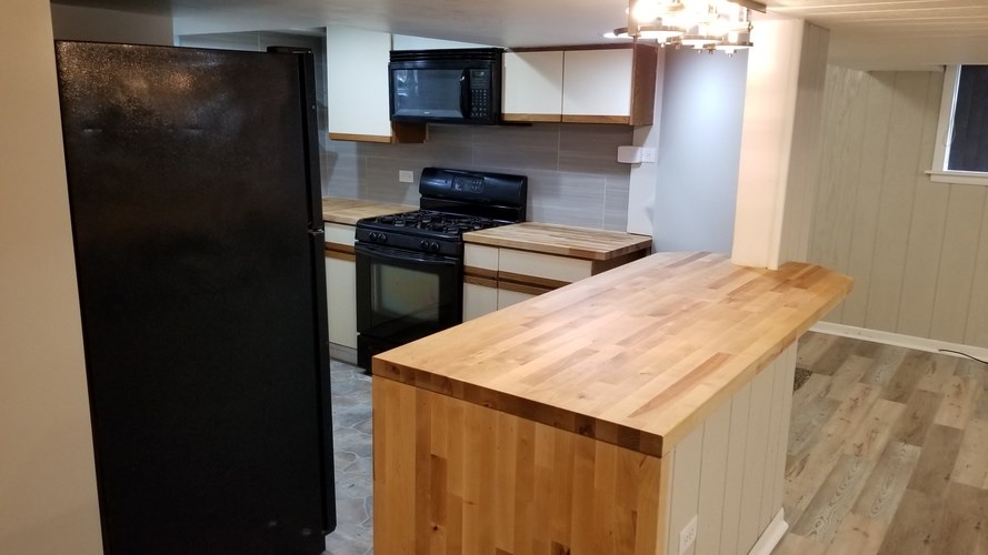 A kitchen with a black refrigerator and wooden countertop.