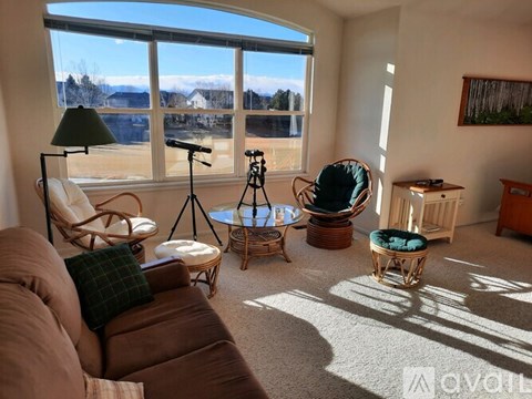 A living room with a brown couch, a chair, a stool, and a table with a tripod and a camera on it.