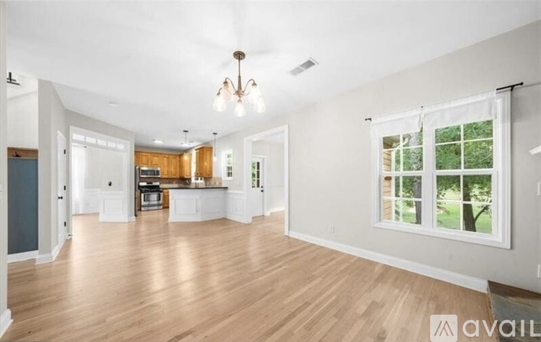 A spacious living room with hardwood floors and a large window overlooking a green outdoor area.