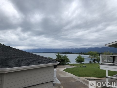 A house with a view of a lake and mountains under a cloudy sky.
