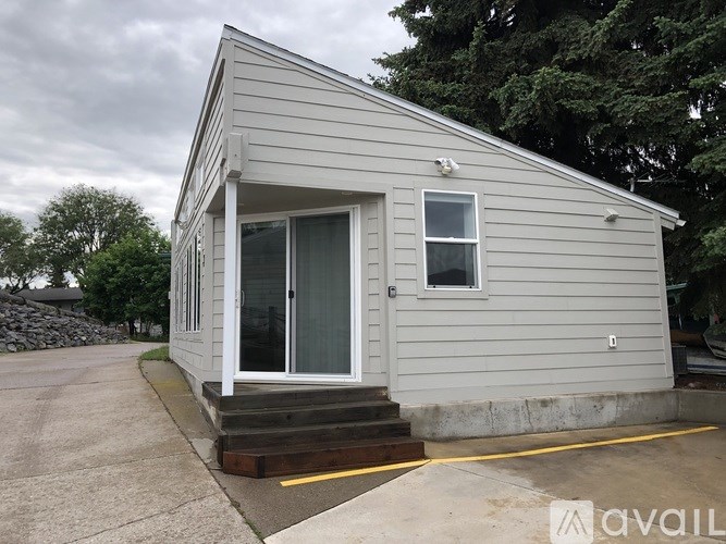 A small house with a grey siding and a white door is available for rent.