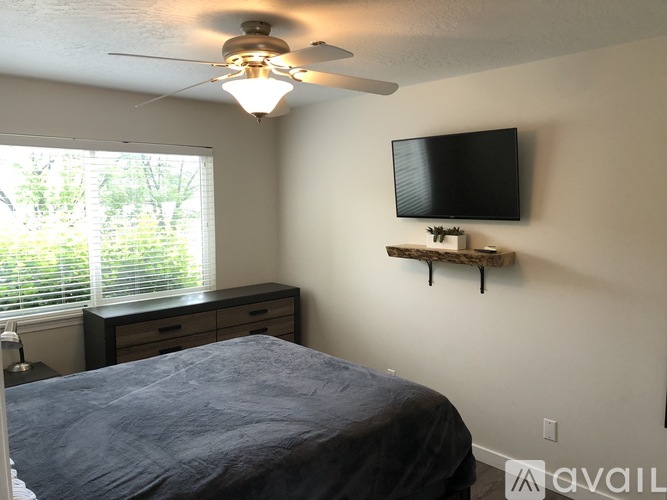 A bedroom with a bed, a ceiling fan, and a television mounted on the wall.